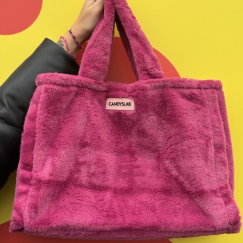 Borsa di pelliccia sintetica di colore magenta con targhetta a marchio Candyslab tenuta su da una mano e indossati al braccio ci sono i bracciali di Candyslab con perline colorate e charm icone foto contestualizzata