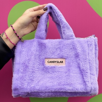 Borsetta di pelliccia sintetica di colore lilla con targhetta a marchio Candyslab tenuta su da una mano e indossati al braccio ci sono i bracciali di Candyslab con perline colorate e charm icone foto contestualizzata